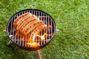 26398106 sausages grilling over the hot glowing coals in a portable barbecue standing on a green lawn with Sausages on the Lawn